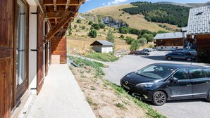Ein Holzgebäude mit überdachter Außenbereich, einem Parkplatz mit Autos und einer hügeligen Landschaft im Hintergrund.