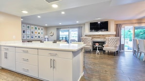 A modern kitchen with a large island, a fireplace, and a TV mounted above it. There are framed pictures on the wall and a dining area with chairs. - 🌴2 King Suites, Huge HEATED POOL& SPA, 8 MIN TO OLD TOWN,2 LIVING ROOMS, FIREPIT (Scottsdale)