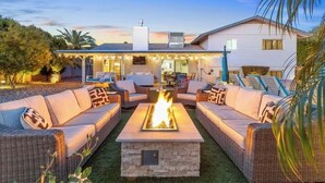 A patio with wicker furniture, a stone fire pit, and a white house in the background. - 🌴2 King Suites, Huge HEATED POOL& SPA, 8 MIN TO OLD TOWN,2 LIVING ROOMS, FIREPIT (Scottsdale)