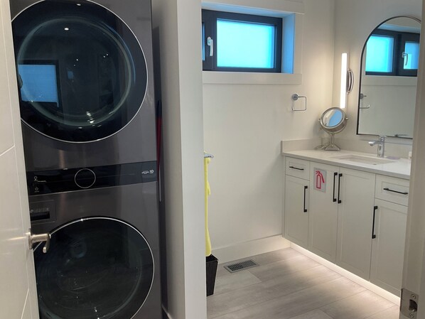 Une salle de bain moderne équipée d’un lave-linge et d’un sèche-linge intégrés, d’une fenêtre, d’un lavabo avec un miroir et de toilettes.