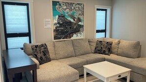 A modern living room with a grey sectional sofa, a white coffee table, and a framed artwork of a train on the wall.