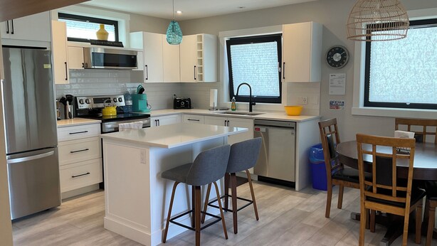 A modern kitchen with a central island, stainless steel appliances, and a dining area with wooden chairs.
