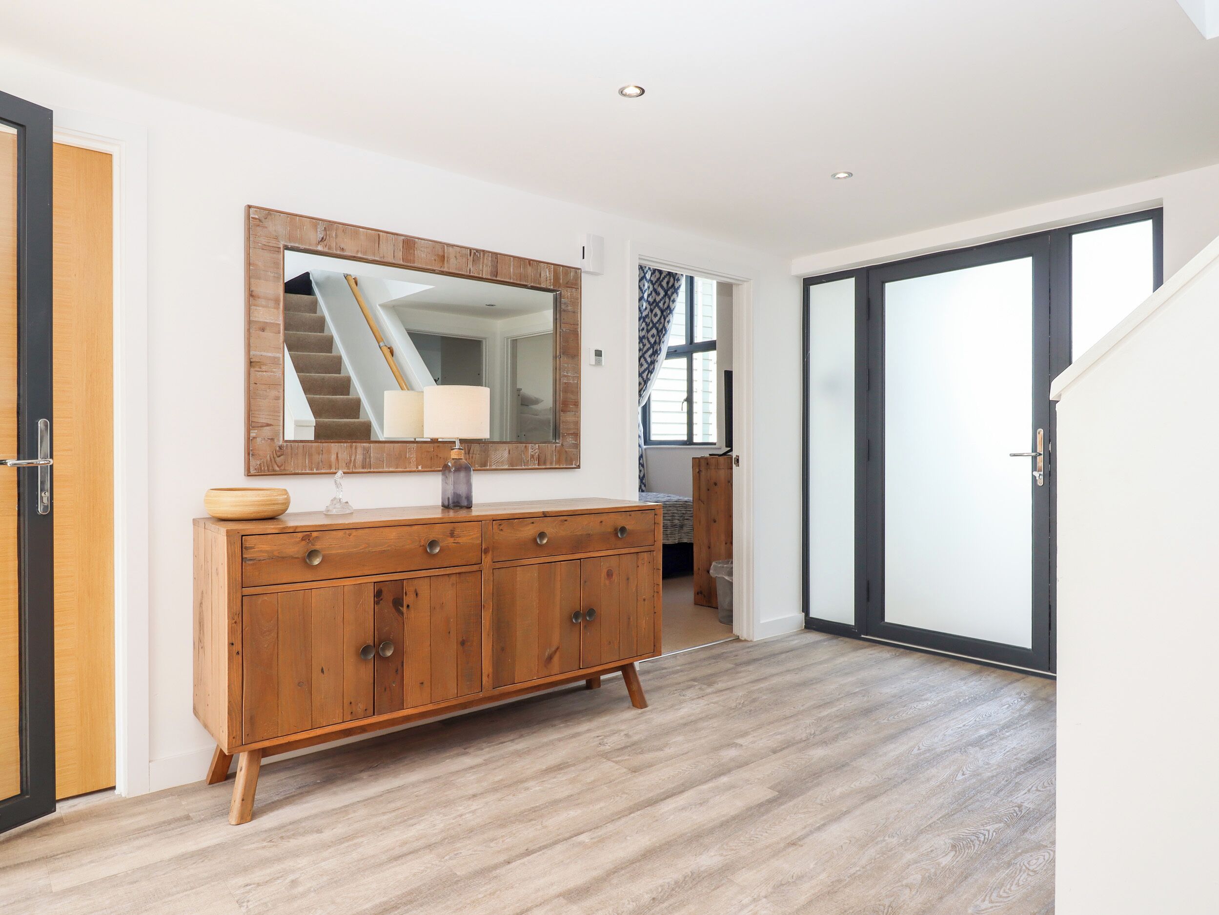 A hallway with a wooden cabinet, a mirror, and a staircase leading to another room.
