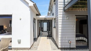 Ein schmaler Weg führt zu einem modernen Haus mit Garage und einer überdachten Sitzgelegenheit im Freien.