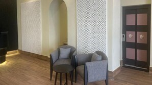 A modern lobby with two grey armchairs, a small table, decorative white panels, and a door with a geometric design. - Ennasma (Casablanca)