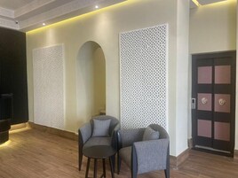 Un vestíbulo moderno con dos sillones grises, una mesita, paneles blancos decorativos y una puerta con diseño geométrico.