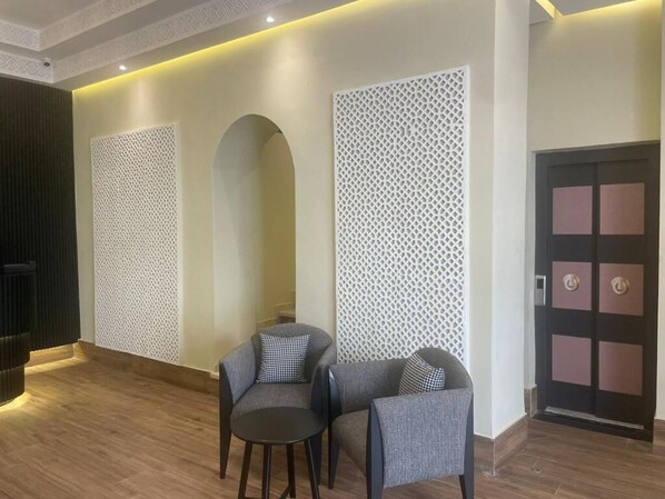 Un vestíbulo moderno con dos sillones grises, una mesita, paneles blancos decorativos y una puerta con diseño geométrico.