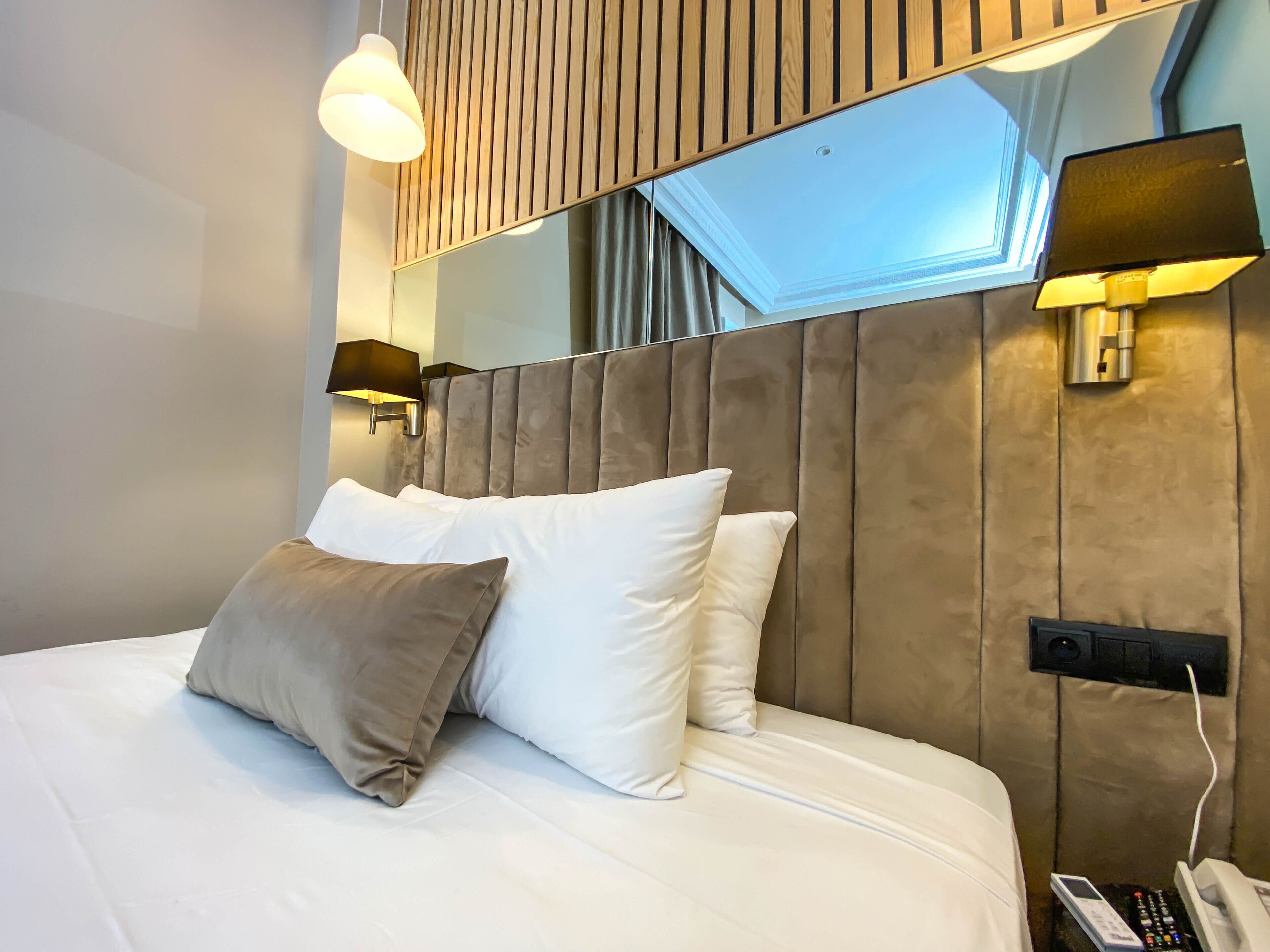A neatly made bed with white and beige pillows, a wooden headboard, and a wall-mounted lamp.
