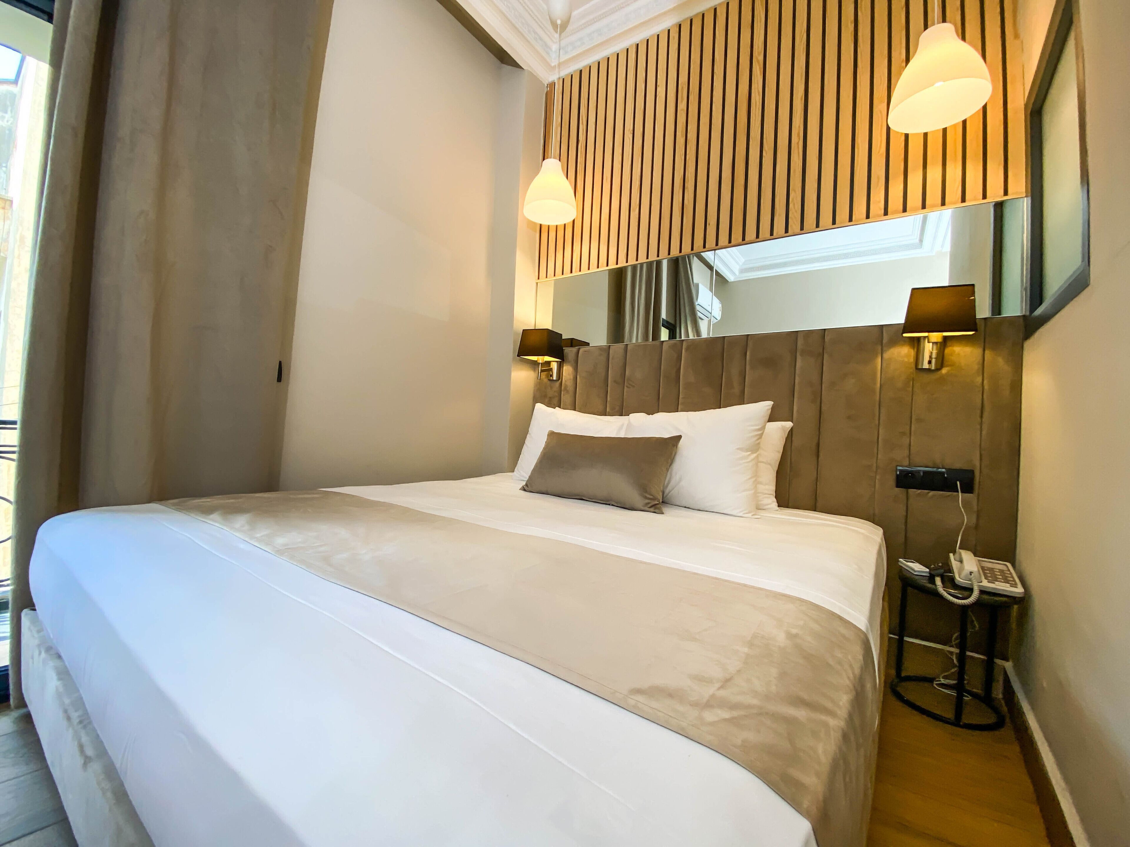 A hotel room with a large bed, two bedside lamps, a bedside telephone, and a mirror above the bed.