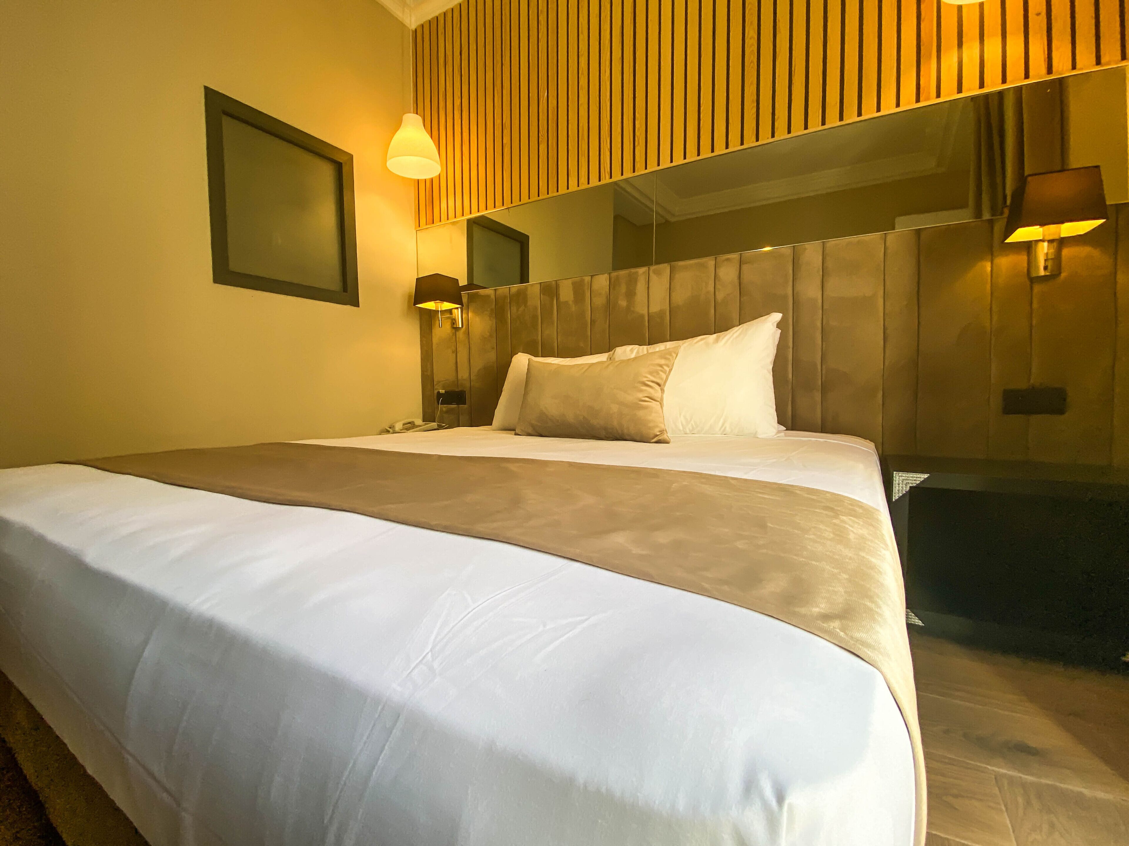 Ein Hotelzimmer mit einem großen Bett, einem hölzernen Kopfteil, zwei Nachttischlampen und einem Spiegel über dem Bett.