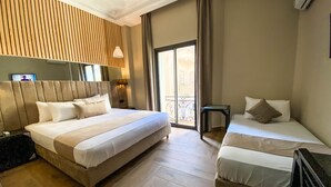 A hotel room with two beds, a wooden headboard, a small table, and a balcony with a view. - Ennasma (Casablanca)