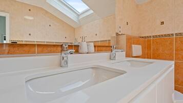 A modern bathroom with two sinks, a skylight, and a large mirror.