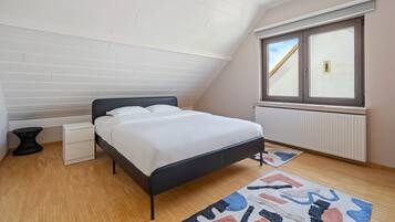 A bedroom with a bed, a window, a radiator, and a ceiling with wooden panels.
