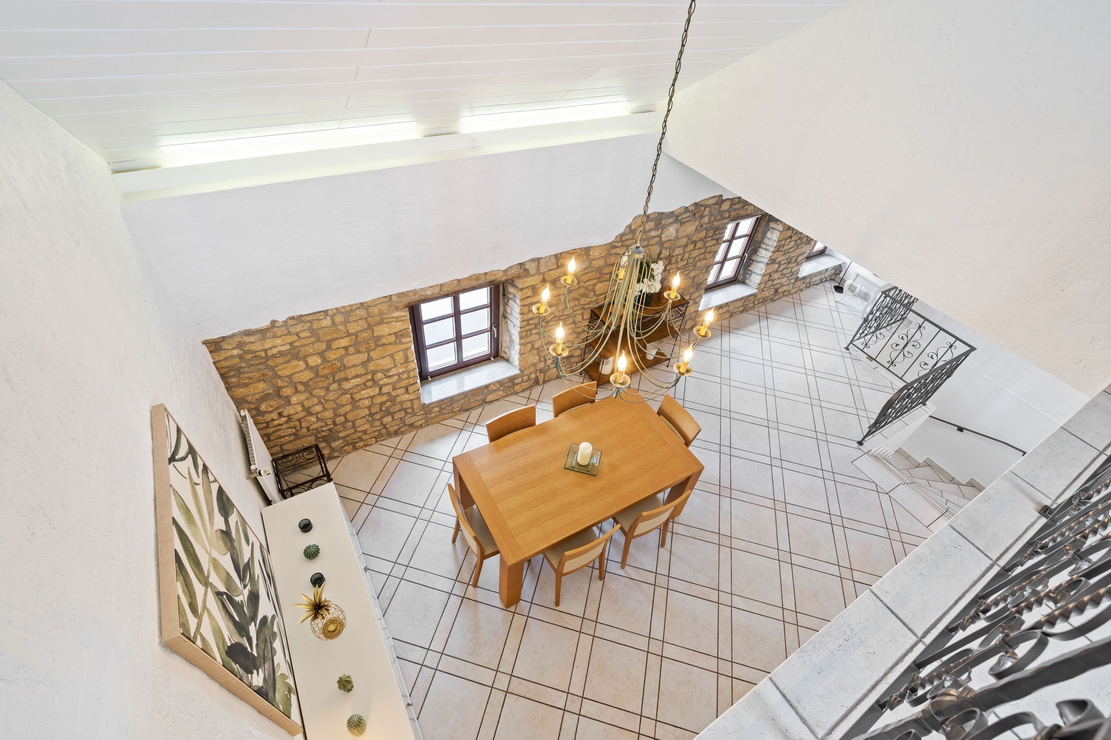 A dining area with a wooden table and chairs, a chandelier, and a stone wall with windows.
