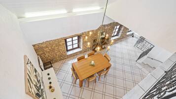 A dining area with a wooden table and chairs, a chandelier, and a stone wall with windows.