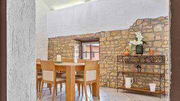 A dining area with a stone wall, a wooden table with chairs, a metal console table with decorative items, and a chandelier.