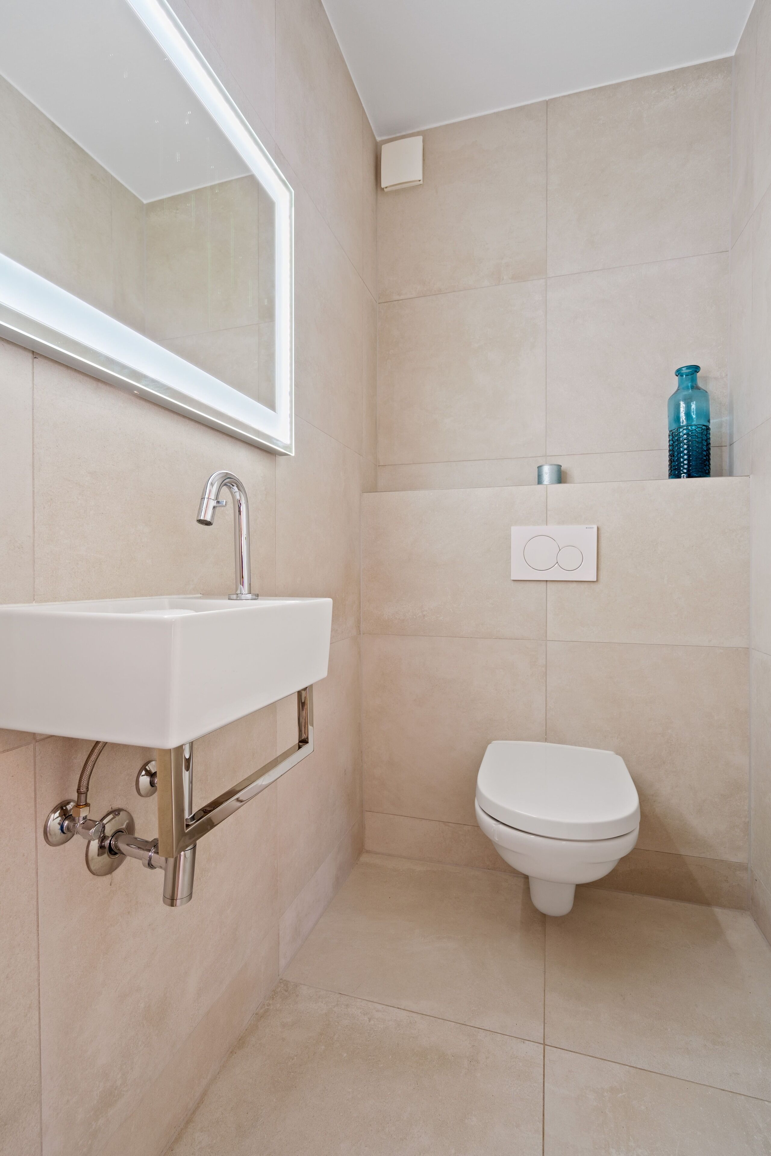 A modern bathroom with a white sink, a mirror, a toilet, and a towel rack.