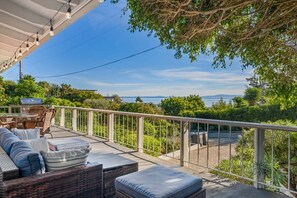 A covered outdoor seating area with wicker furniture, a grill, and a view of the sea.