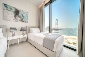 Una habitación de hotel moderna con una cama grande, un escritorio con lámparas y vistas a una playa y una noria.