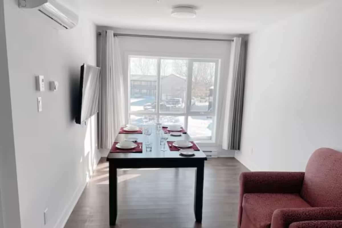 Un coin repas avec une table dressée pour quatre personnes, un canapé rouge et une grande fenêtre avec des rideaux.