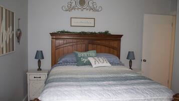 A bedroom with a wooden headboard, a quilted bedspread, two bedside lamps, and a decorative wall piece above the bed.