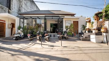A hotel entrance with a covered walkway, parked motorcycles, and a traditional decorative structure.