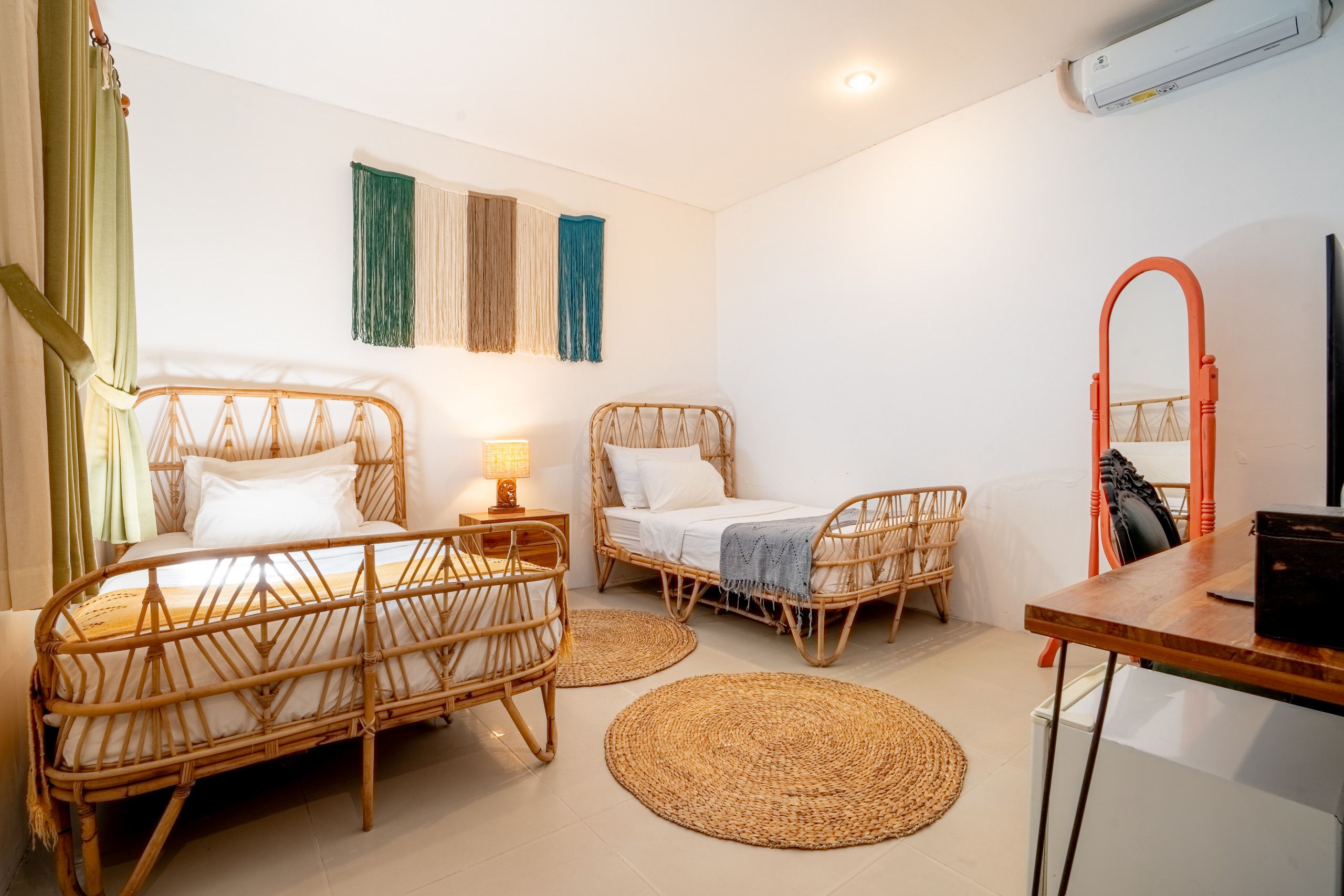 A room with two wicker beds, a wooden table, a mirror, and a wall-mounted air conditioner.