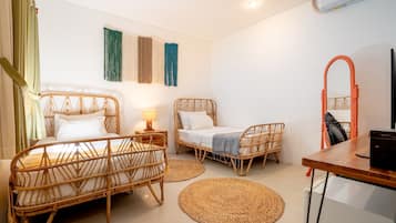 A room with two wicker beds, a wooden table, a mirror, and a wall-mounted air conditioner.