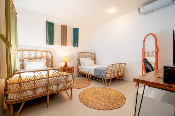 Ein Zimmer mit zwei Korbmöbelbetten, einem Holztisch, einem Spiegel und einer Wandklimaanlage.