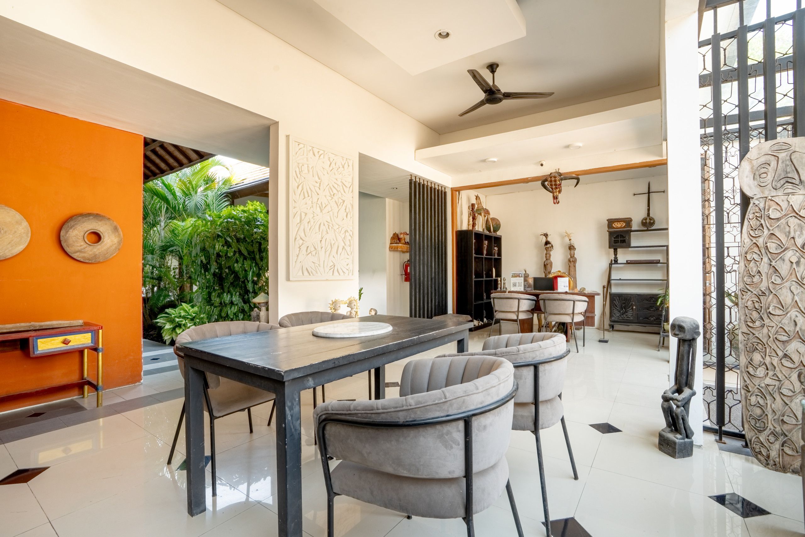 A modern dining area with a black table, grey upholstered chairs, and a ceiling fan.