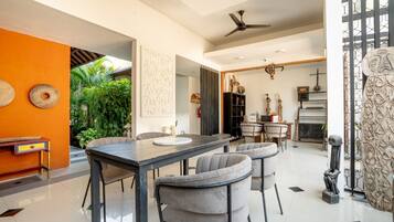 A modern dining area with a black table, grey upholstered chairs, and a ceiling fan.