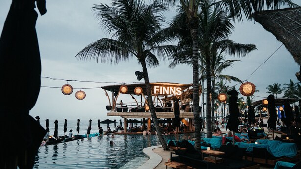A beachfront bar with a pool, palm trees, and outdoor seating. - Seaside Boutique Hotel 102 (30m from beach) (Canggu)