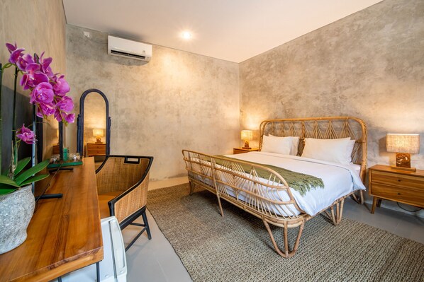 Een slaapkamer met een rieten bed, een bureau met stoel, een potorkidee en een spiegel.