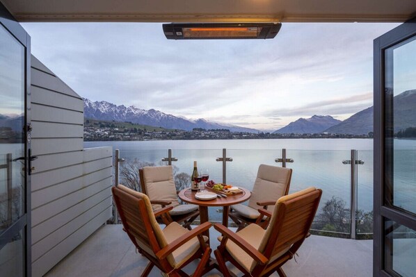 Varanda com mesa posta para dois, com vista para um lago e montanhas.