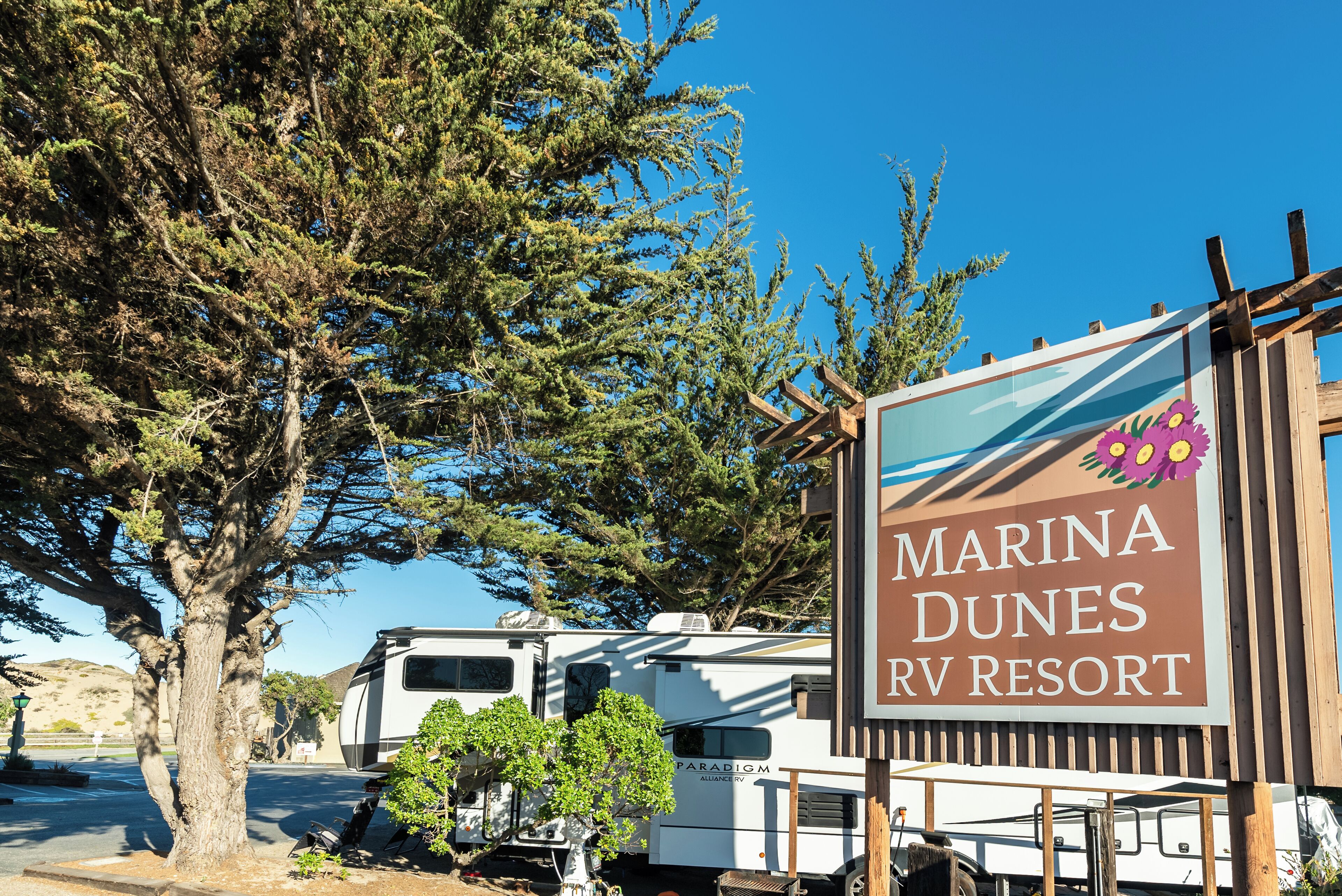 A sign for Marina Dunes RV Resort with RVs parked nearby.