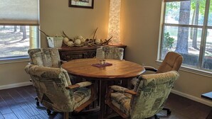 Uma sala de conferências com uma mesa redonda de madeira, cadeiras estampadas, um ventilador de teto e uma janela com vista para árvores.
