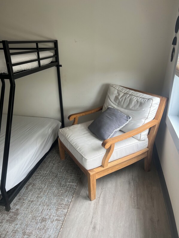 A bunk bed with a wooden chair beside it, both with white cushions.