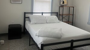Une chambre à coucher avec un lit, une fenêtre, une table de chevet et une étagère fixée au mur.