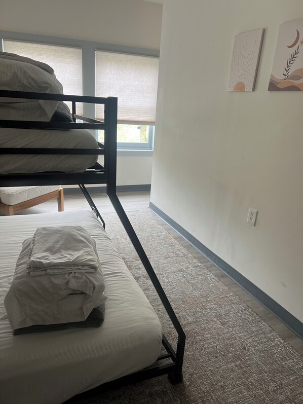 Una habitación con literas, una mesita pequeña y una ventana con persianas.