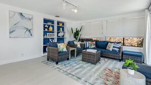 A modern living room with wicker furniture, a blue sofa, and a bookshelf.