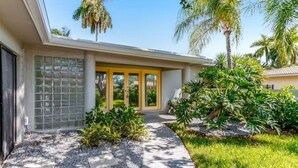 A modern house with a covered entryway, a gravel driveway, and tropical landscaping.
