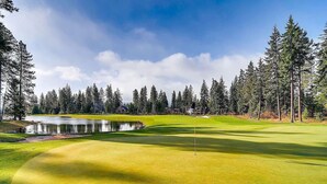 A golf course with a pond, surrounded by tall trees and a clear sky.
