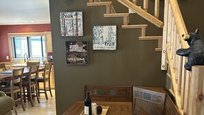 A wooden staircase with a bear figurine, a dining area with a bench and table, and wall art depicting nature scenes.