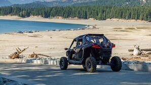 A vehicle on a road with a beach and forest in the background.