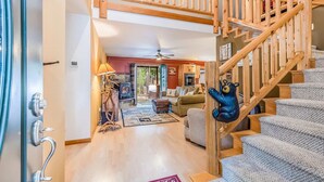 A spacious living area with a high ceiling, a wooden staircase, and a cozy fireplace.