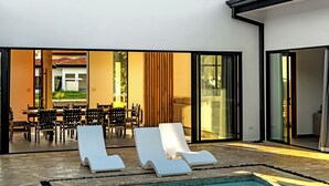 Ein modernes Haus mit Swimmingpool, zwei Liegestühlen und einem Essbereich mit Tisch und Stühlen.