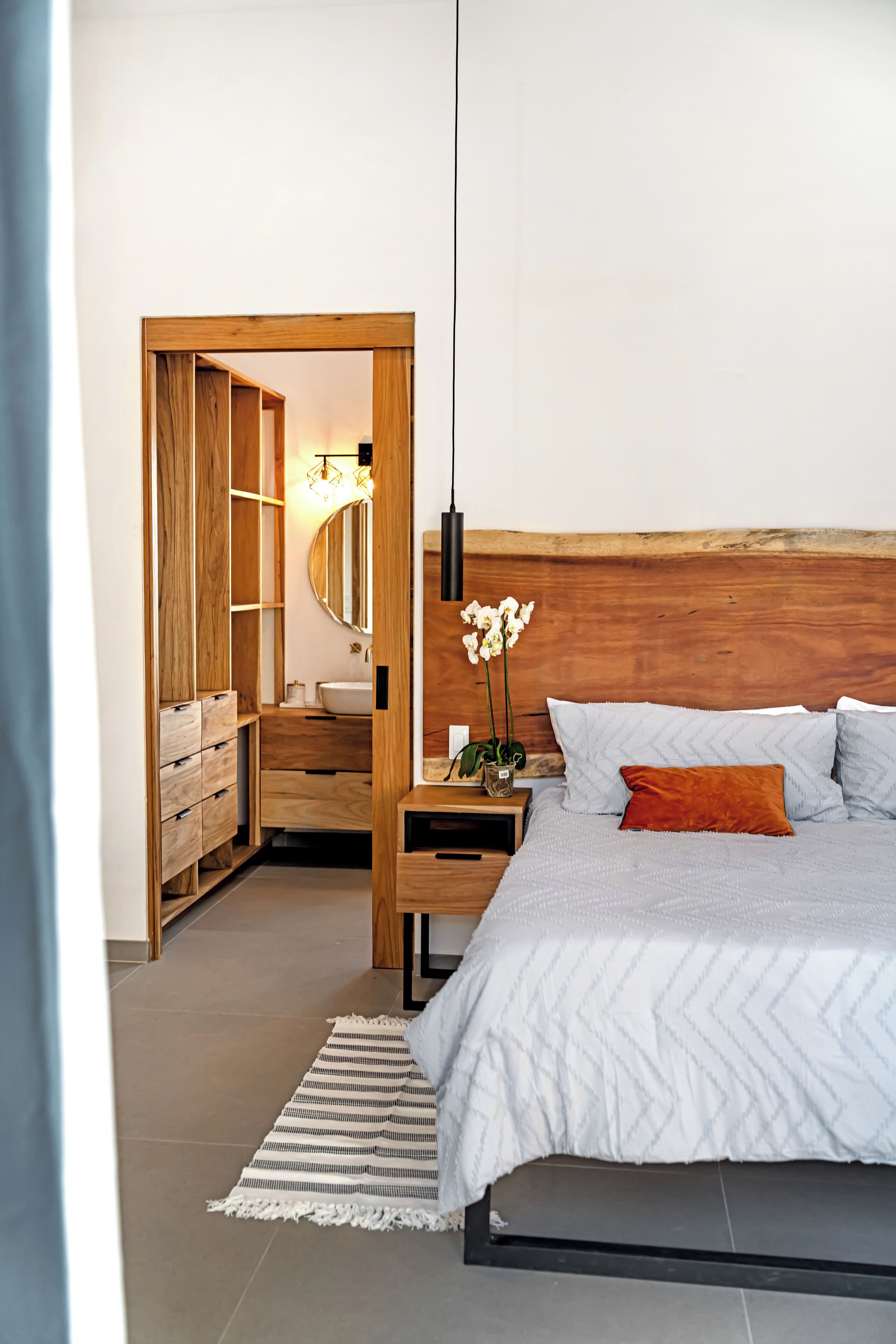 Une chambre à coucher avec une tête de lit en bois, un lit recouvert d’une couette blanche, une table de chevet avec une lampe et une armoire en bois.