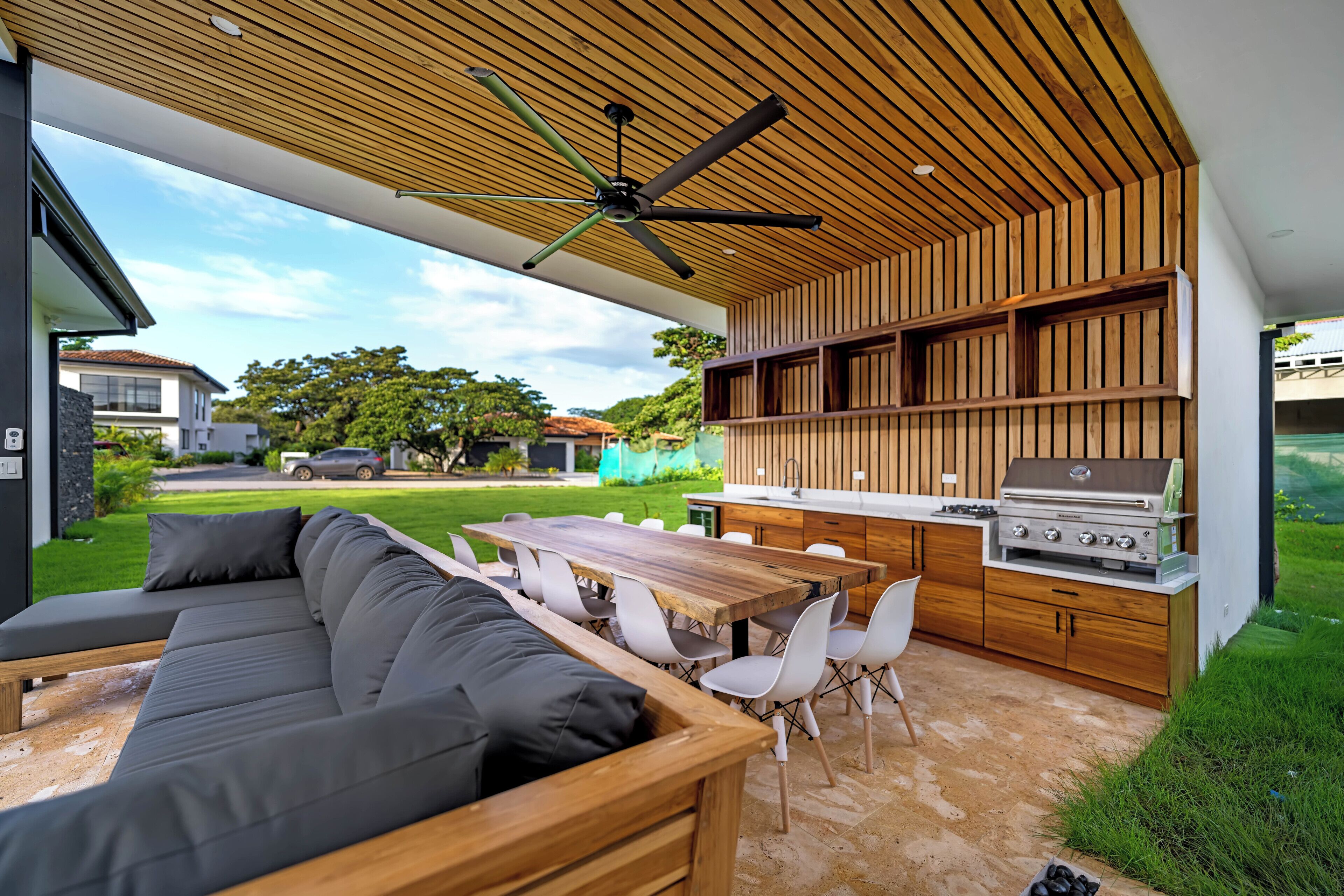 Een terras buiten met een houten dak, een ingebouwde barbecue en een eethoek met stoelen en een tafel.