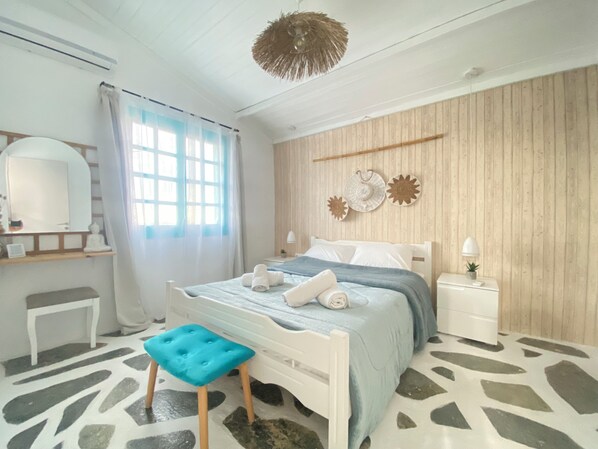 A bedroom with a bed, a nightstand, a chair, a hanging light fixture, and a window with curtains.