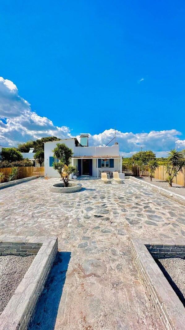 A modern house with a stone patio, a small garden, and a clear blue sky.